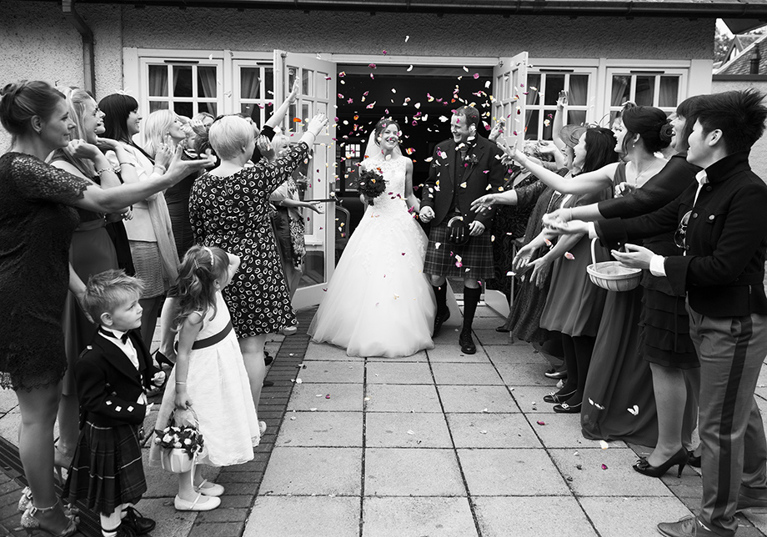 Black and white image of bride and groom walking through confetti